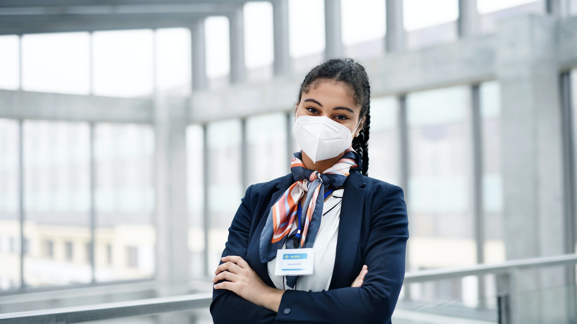 Young air hostess looking at camera in airport lounge, coronavirus, travel and new normal