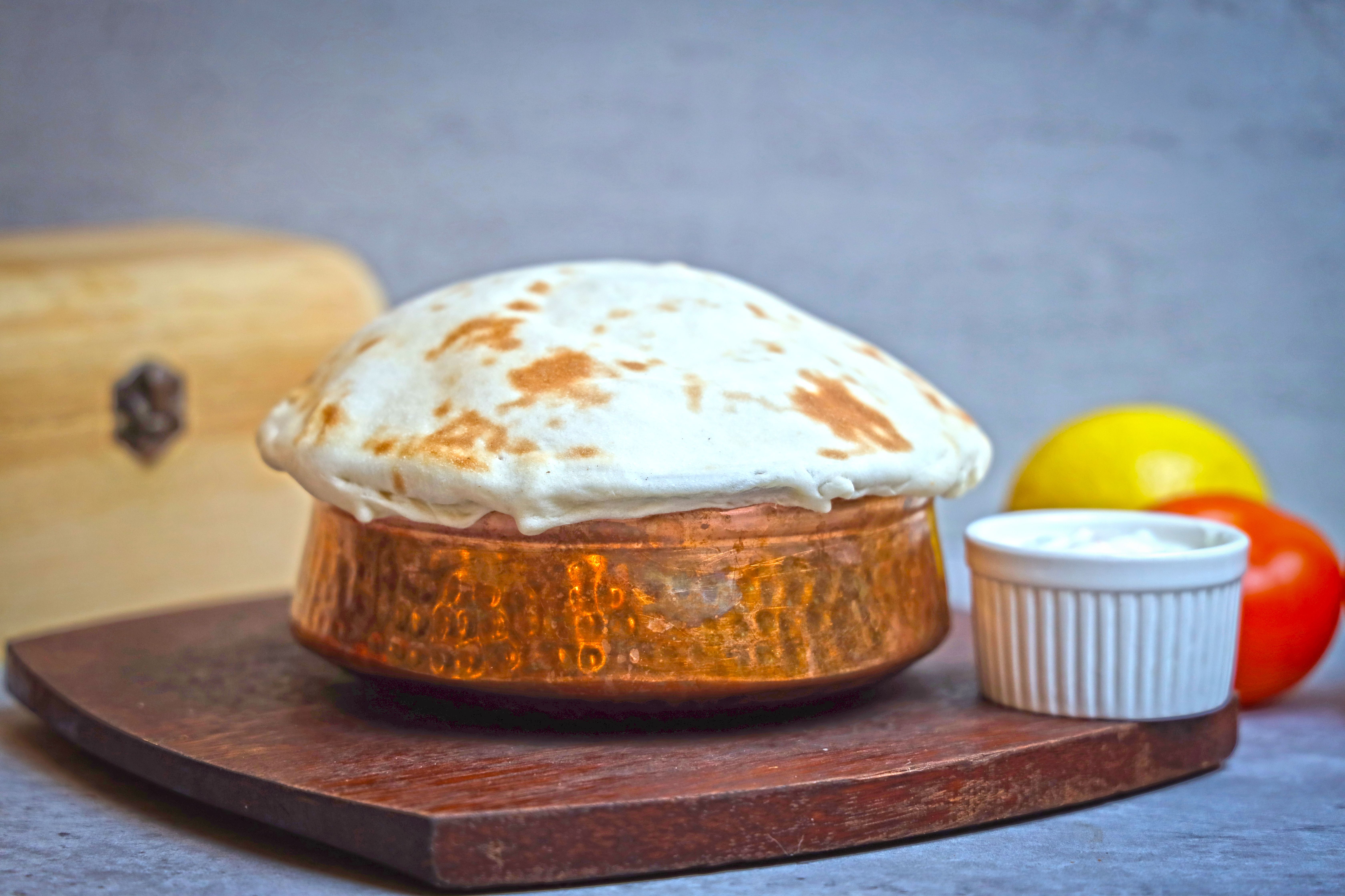 Delicious traditional Indian dish in a hammered copper pot with a dough lid, photographed indoors.