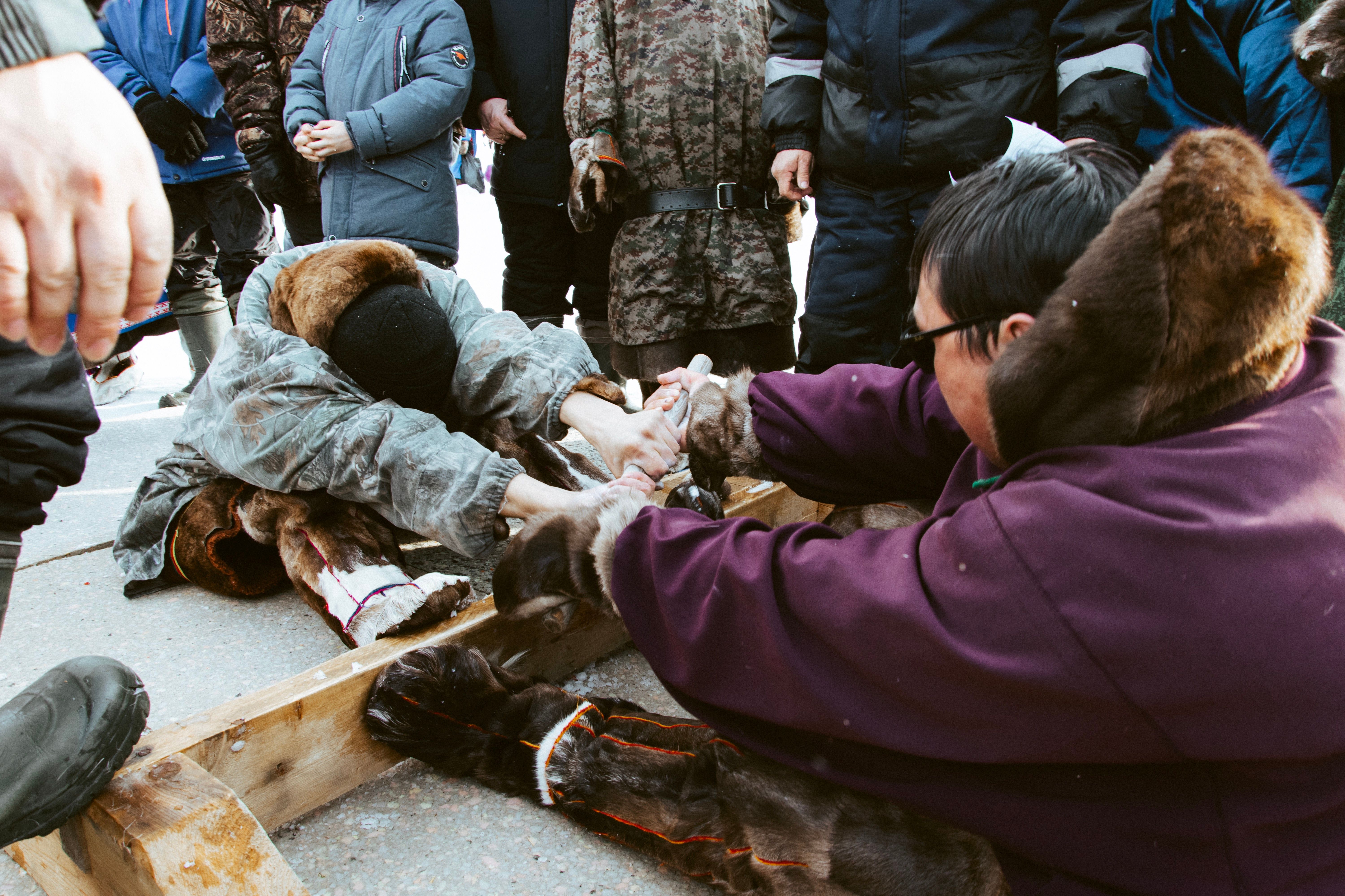 Two people in fur clothing engage in a traditional grappling contest during winter.
