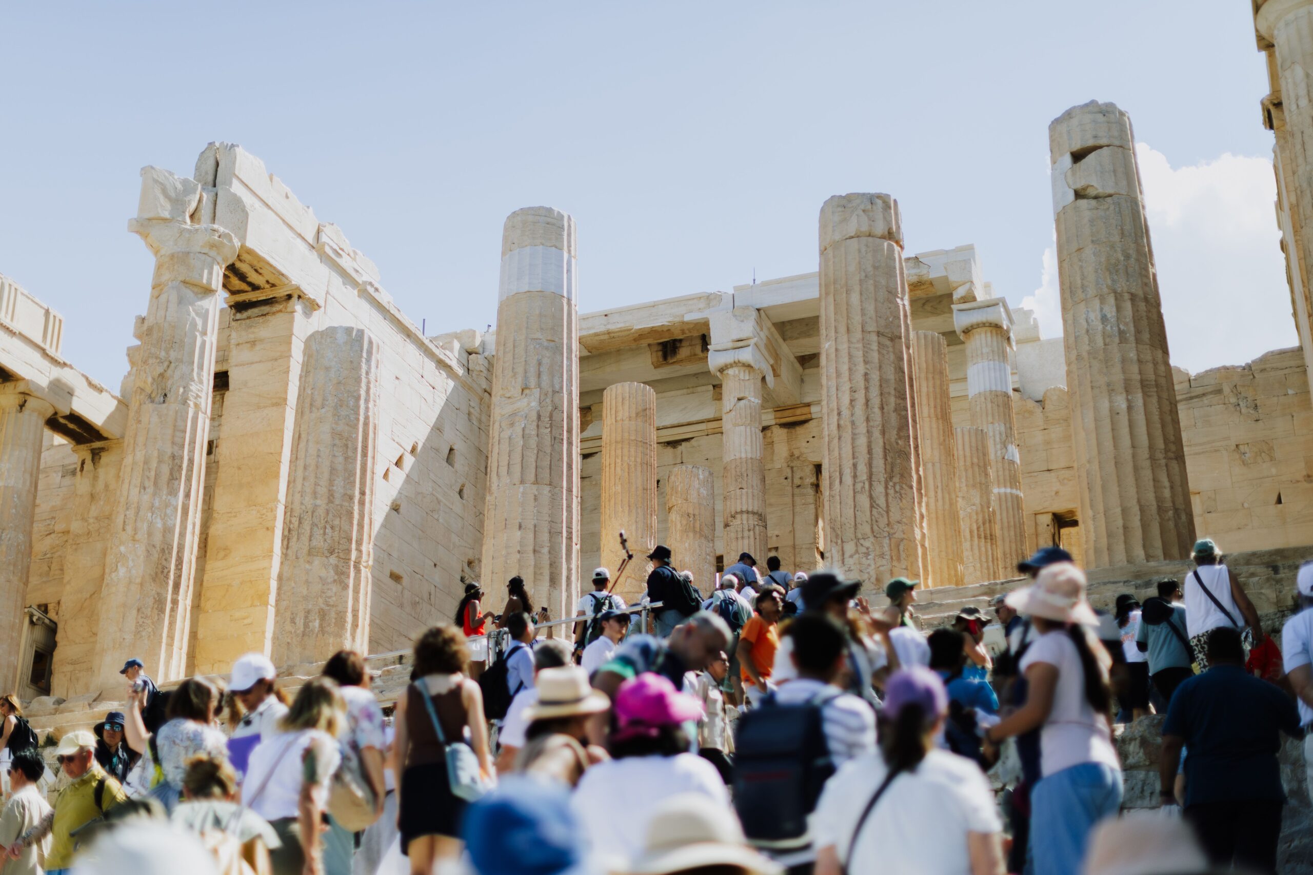Crowds of tourists visiting the ancient Parthenon in Athens, Greece, under a clear blue sky.